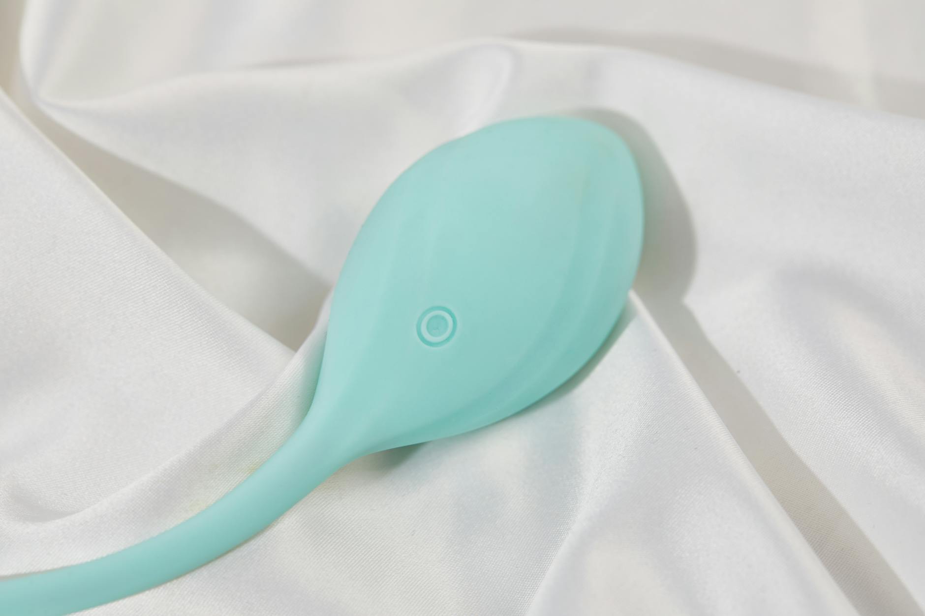 A sleek teal lemon clitoral vibrator on soft white silk fabric