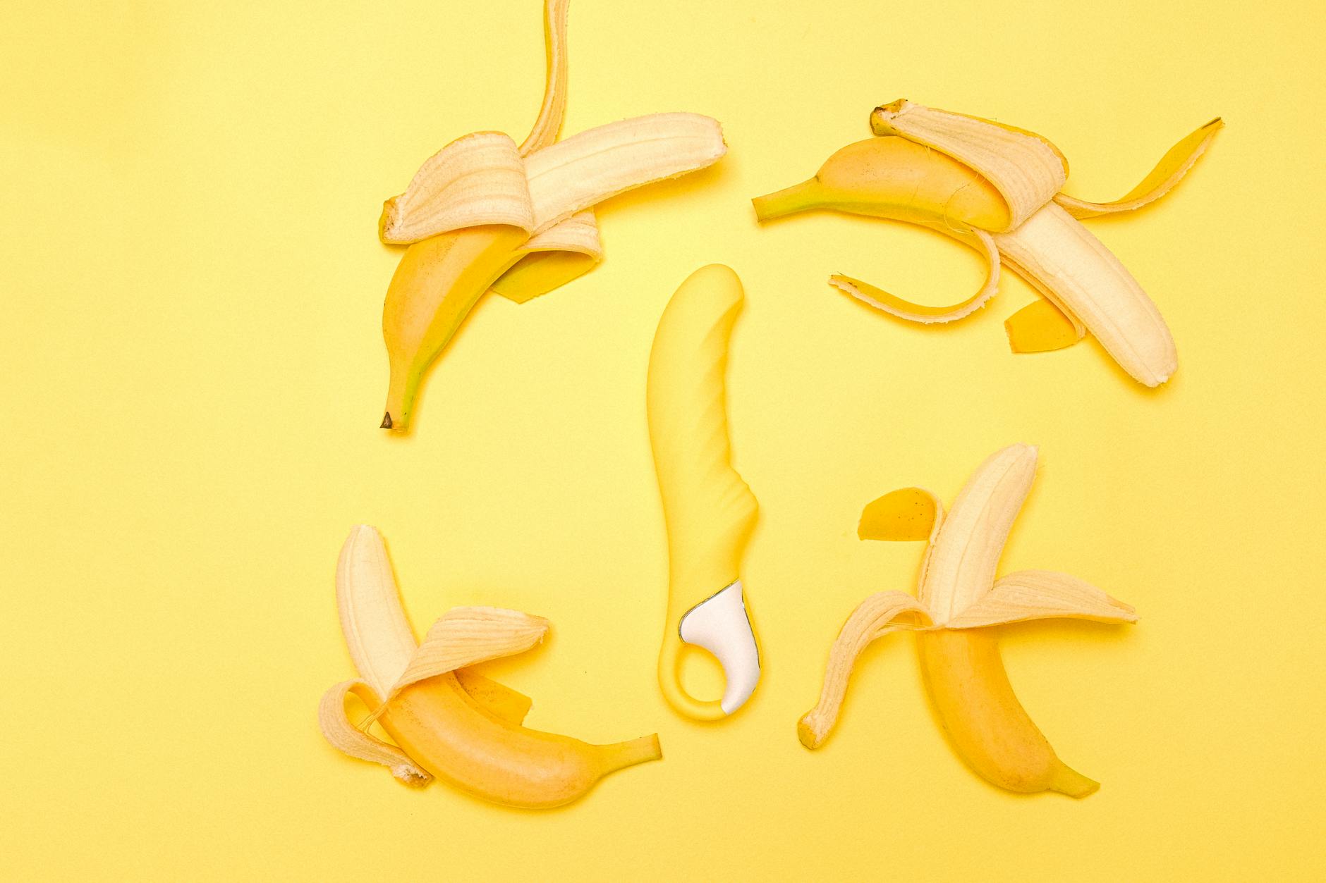 A yellow Lemon Clit Massager vibrator surrounded by fresh peeled bananas on a bright yellow background