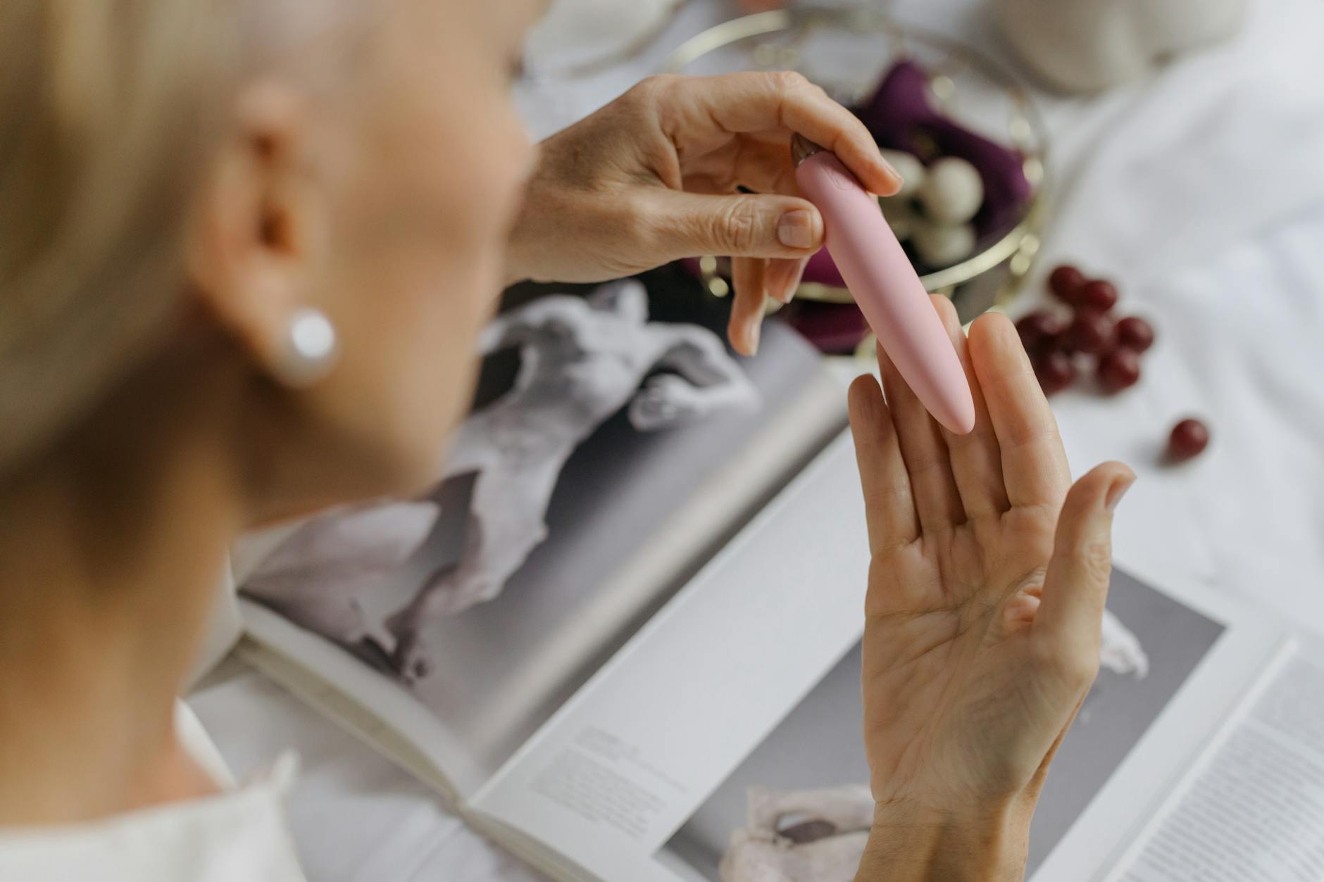 Una mano con uñas blancas sosteniendo un limón fresco sobre un fondo rosa suave