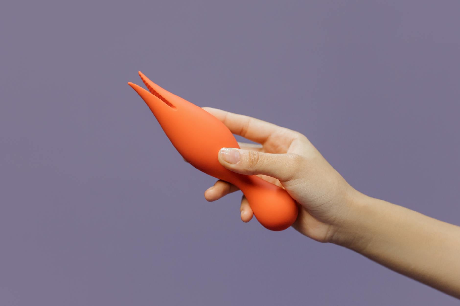 Primer plano de una mano sosteniendo un vibrador naranja moderno contra un fondo minimalista, mostrando sensualidad contemporánea