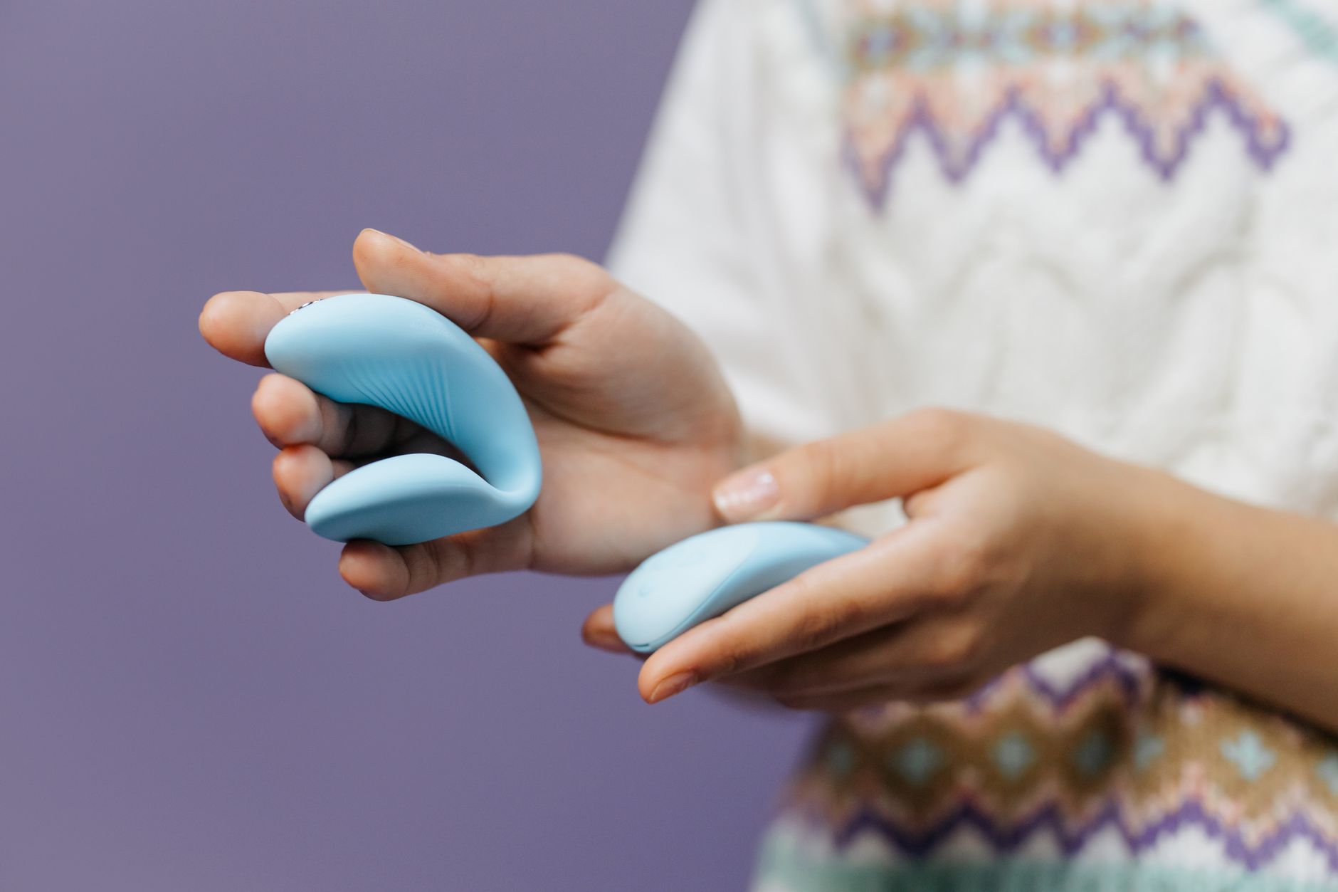 Pareja íntima sosteniéndose con un vibrador azul contra un fondo púrpura minimalista.