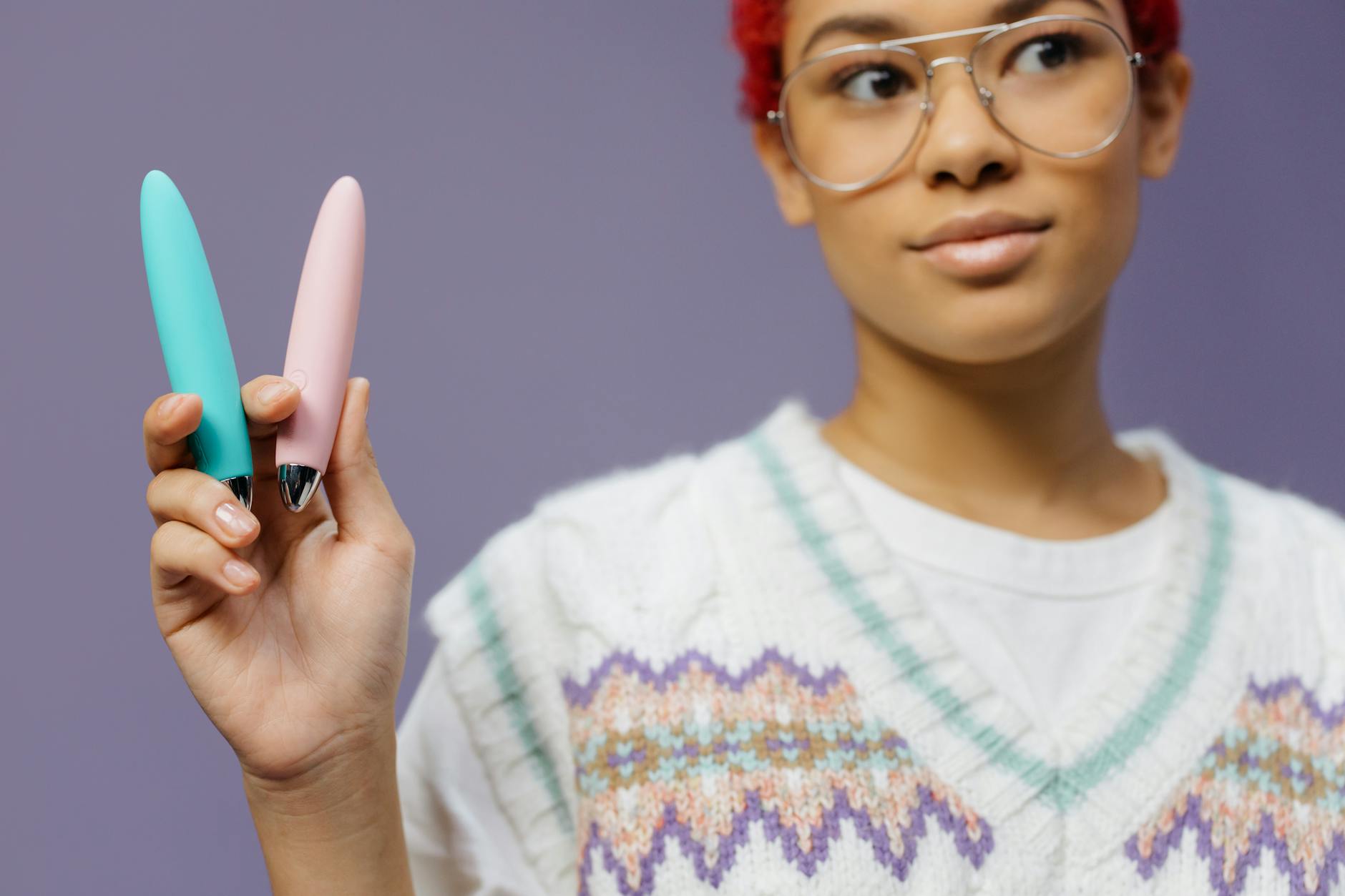 Woman holding colorful vibrators against a purple background, representing sexual wellness and personal choice.