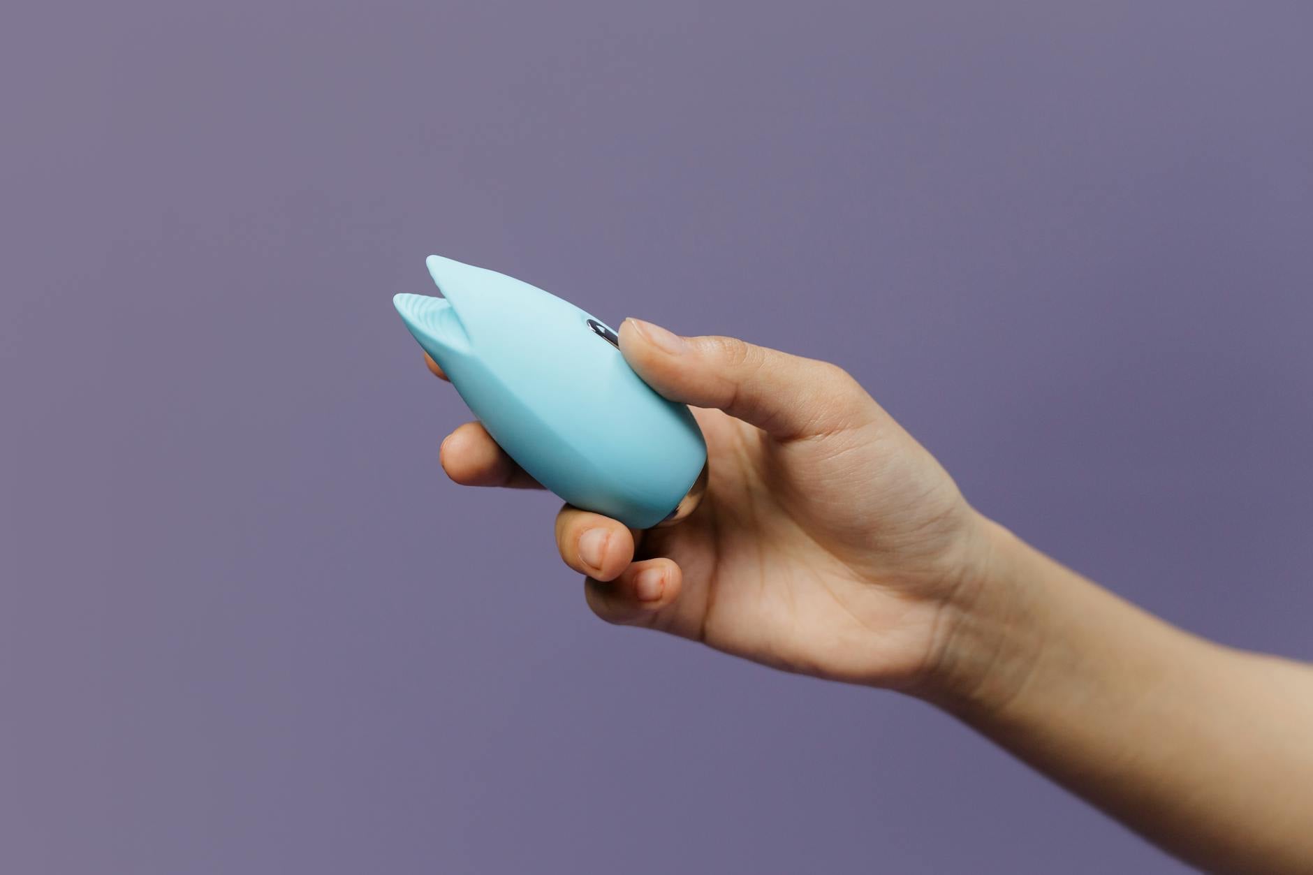 Una mujer sosteniendo un vibrador rosa en primer plano, con libros de arte de fondo, enfatizando temas íntimos y personales.