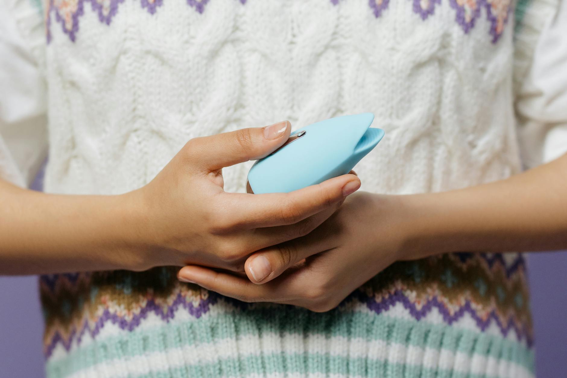 Close-up of hands holding a blue lemon clitoral vibrator against a knitted sweater