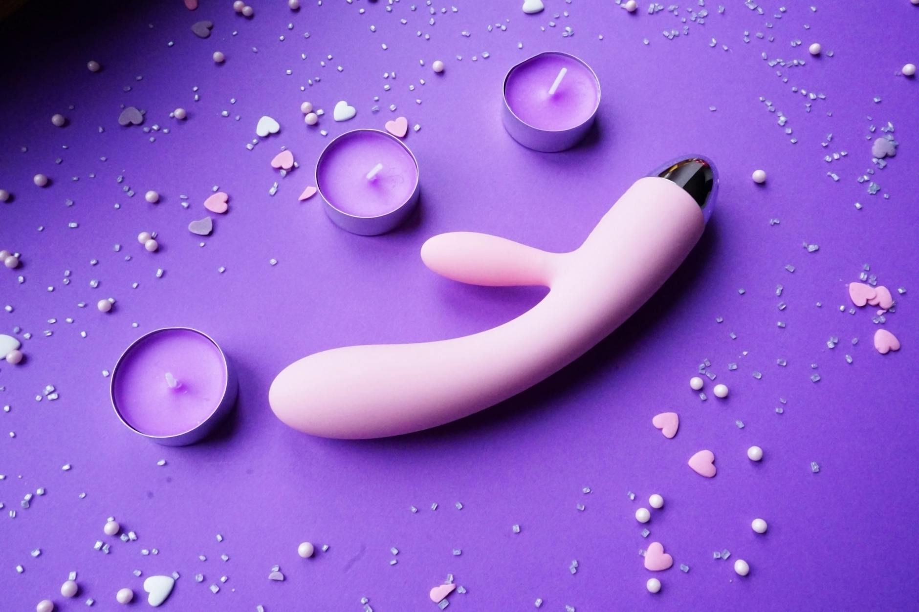 Vibrador de limón rosa sobre fondo púrpura con confeti de corazones y velas para un ambiente romántico